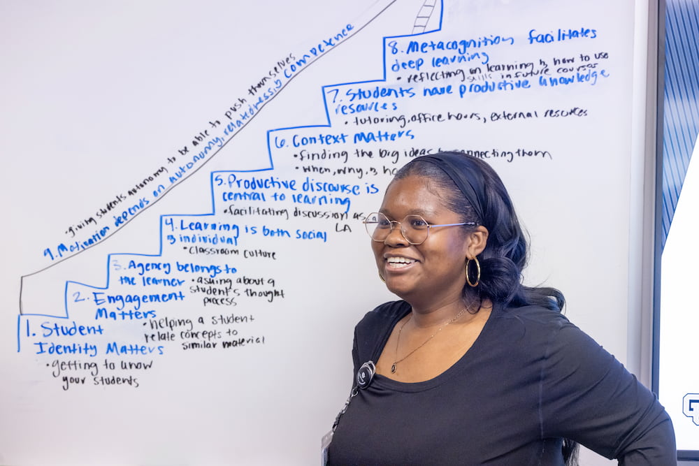 A CU Denver student draws on the whiteboard, explaining STEM Ed learning processes