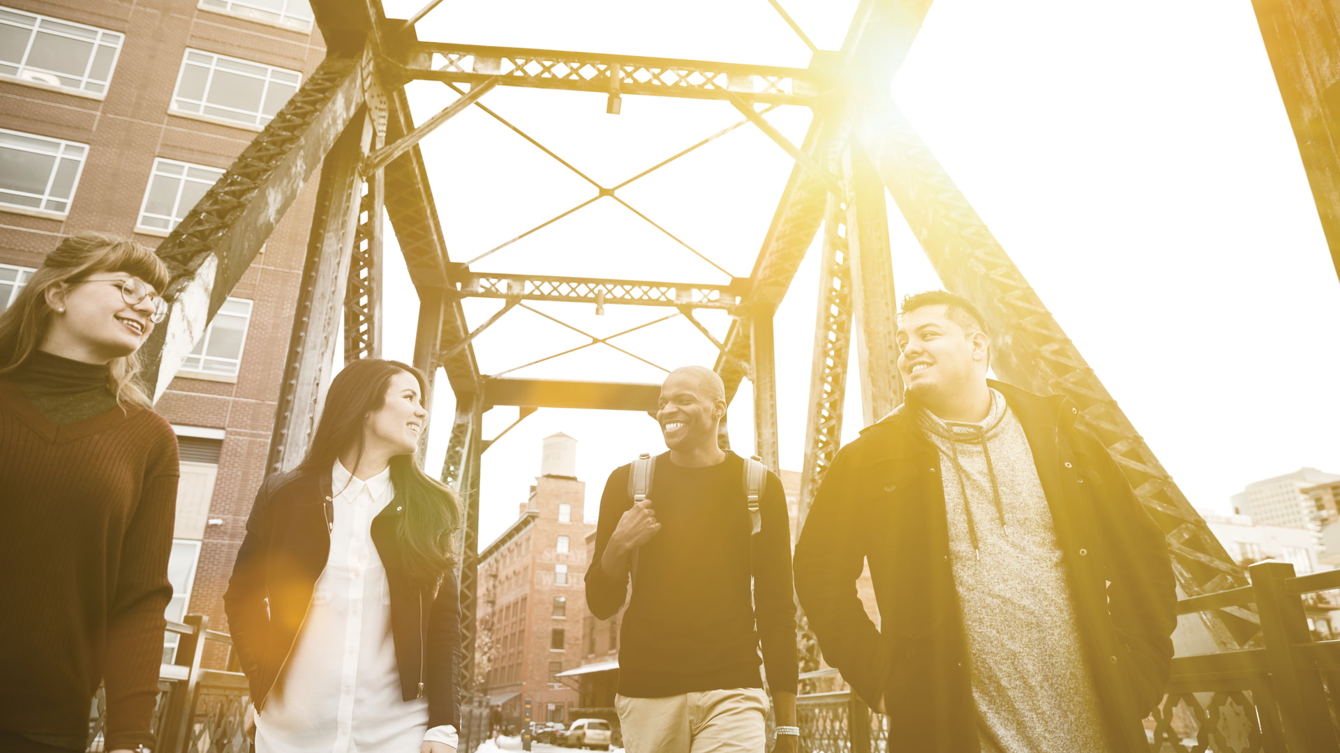 4 students walk across a bridge and smile at each other